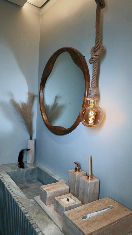 Detalhe de torneira, cuba de pedra e espelho oval iluminado