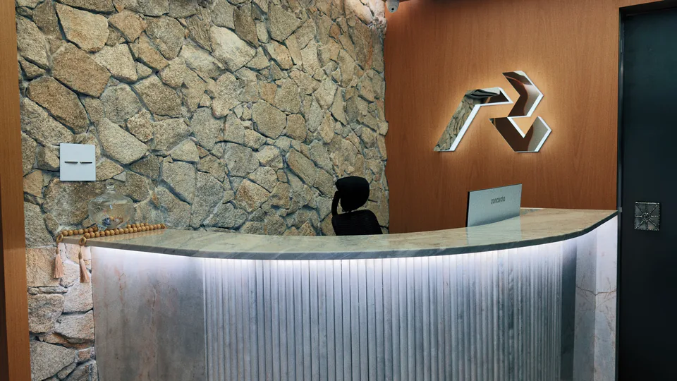 Recepção do Instituto com balcão curvo, parede de pedra e símbolo iluminado