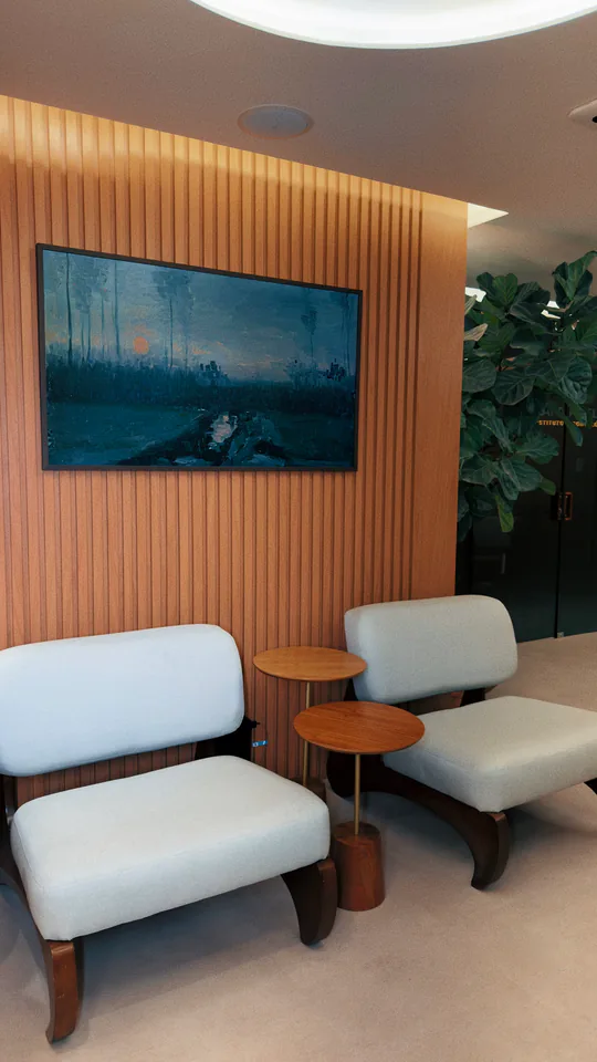 Sala de espera com poltronas claras, madeira e obra de arte