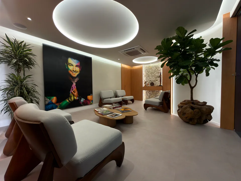 Sala de espera com poltronas claras, retrato de Rafa Puglisi e nicho de pedra iluminado