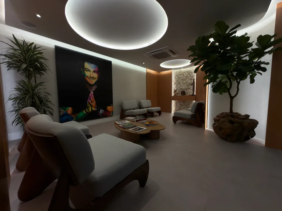 Sala de espera fotografada a partir de uma poltrona, com retrato de Rafa Puglisi ao fundo