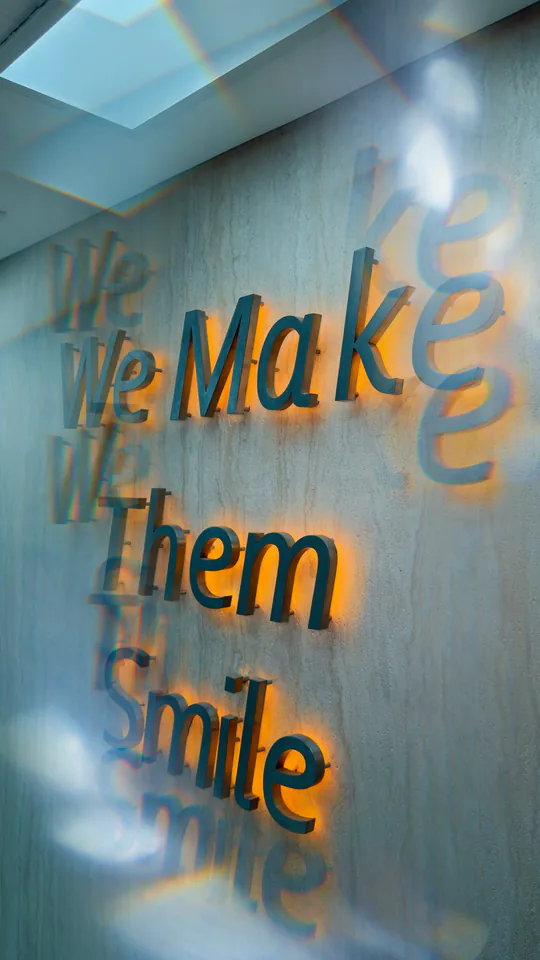Frase We Make Them Smile iluminada sobre parede de pedra