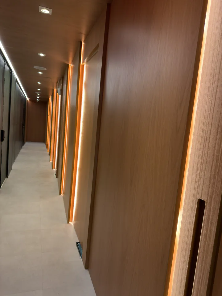 Perspectiva do corredor com iluminação linear entre os painéis de madeira