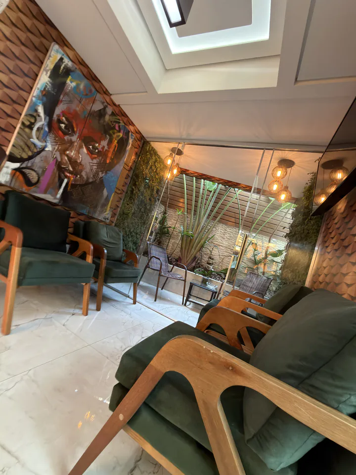 Lounge com poltronas verdes, obra de arte e jardim visível pelas portas de vidro
