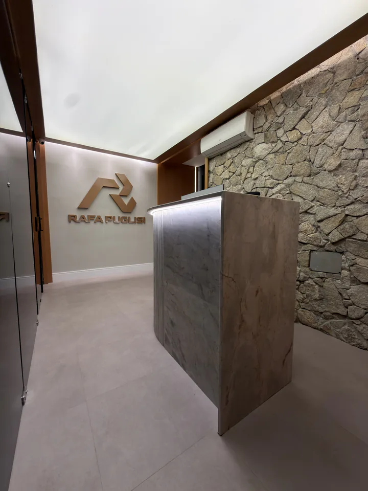 Balcão da recepção diante da parede de pedra e da marca Rafa Puglisi