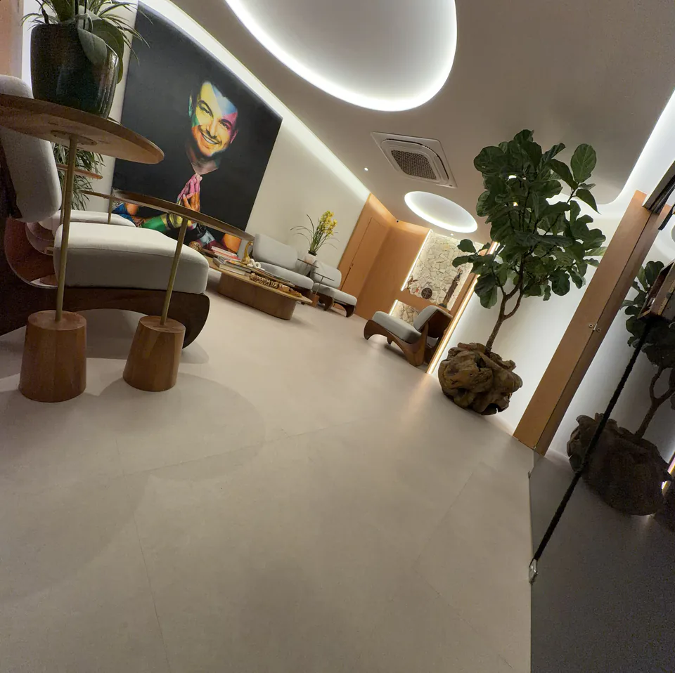 Sala de espera enquadrada a partir da circulação com mesas, poltronas e vegetação