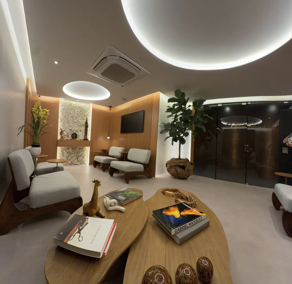 Vista ampla da sala de espera com mesas centrais, poltronas e entrada de vidro