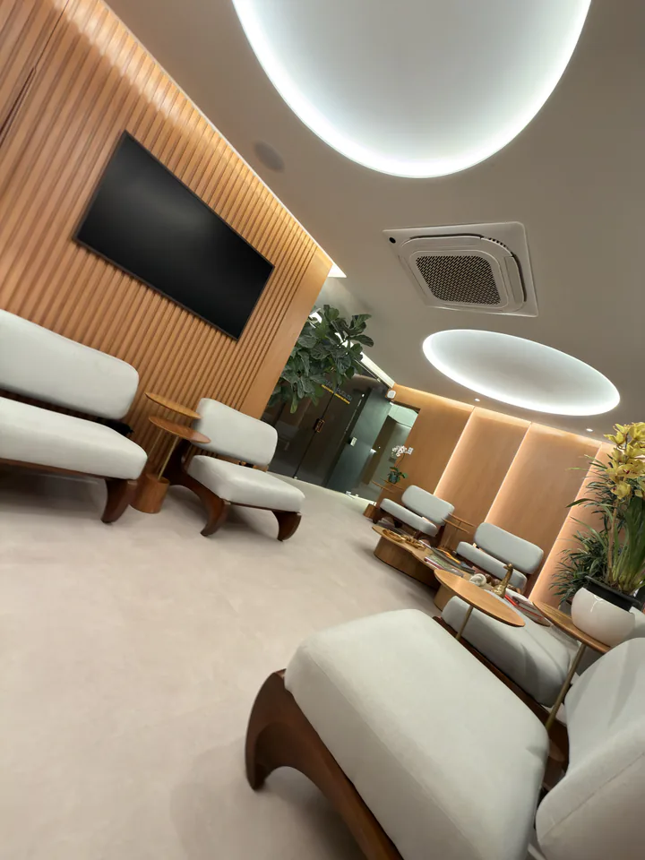 Poltronas claras e painel de madeira vistos junto à mesa central
