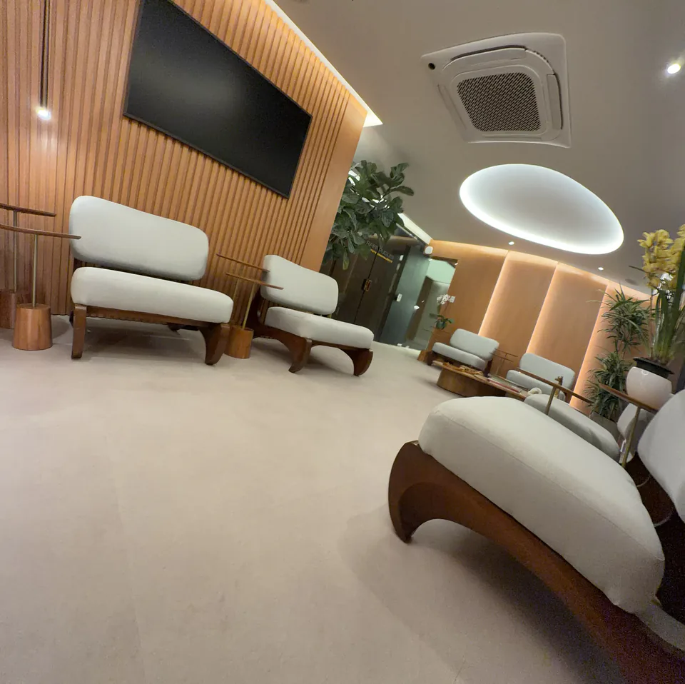 Sala de espera em enquadramento diagonal com poltronas, mesa e plantas