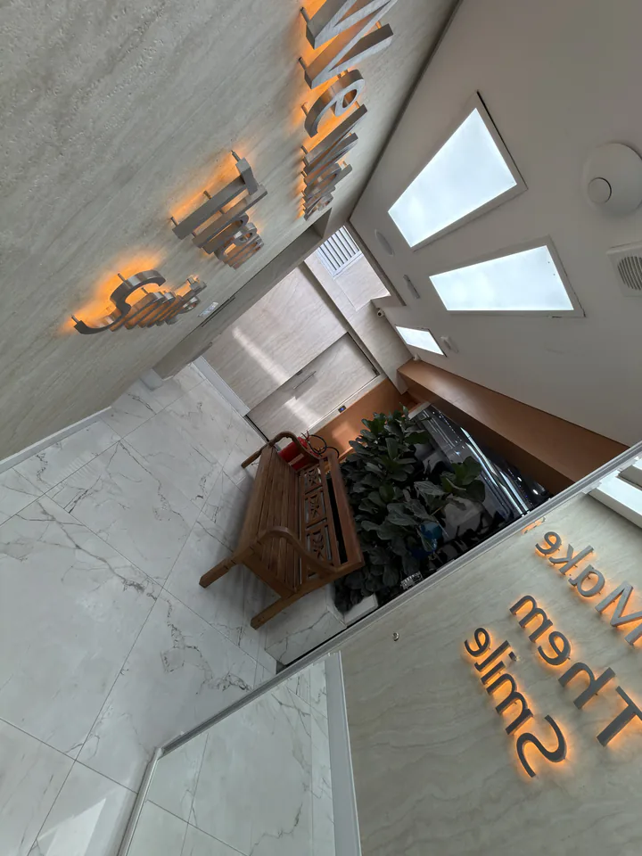 Frase We Make Them Smile iluminada junto a banco de madeira e plantas