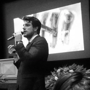 Rafa Puglisi falando ao microfone durante uma palestra.