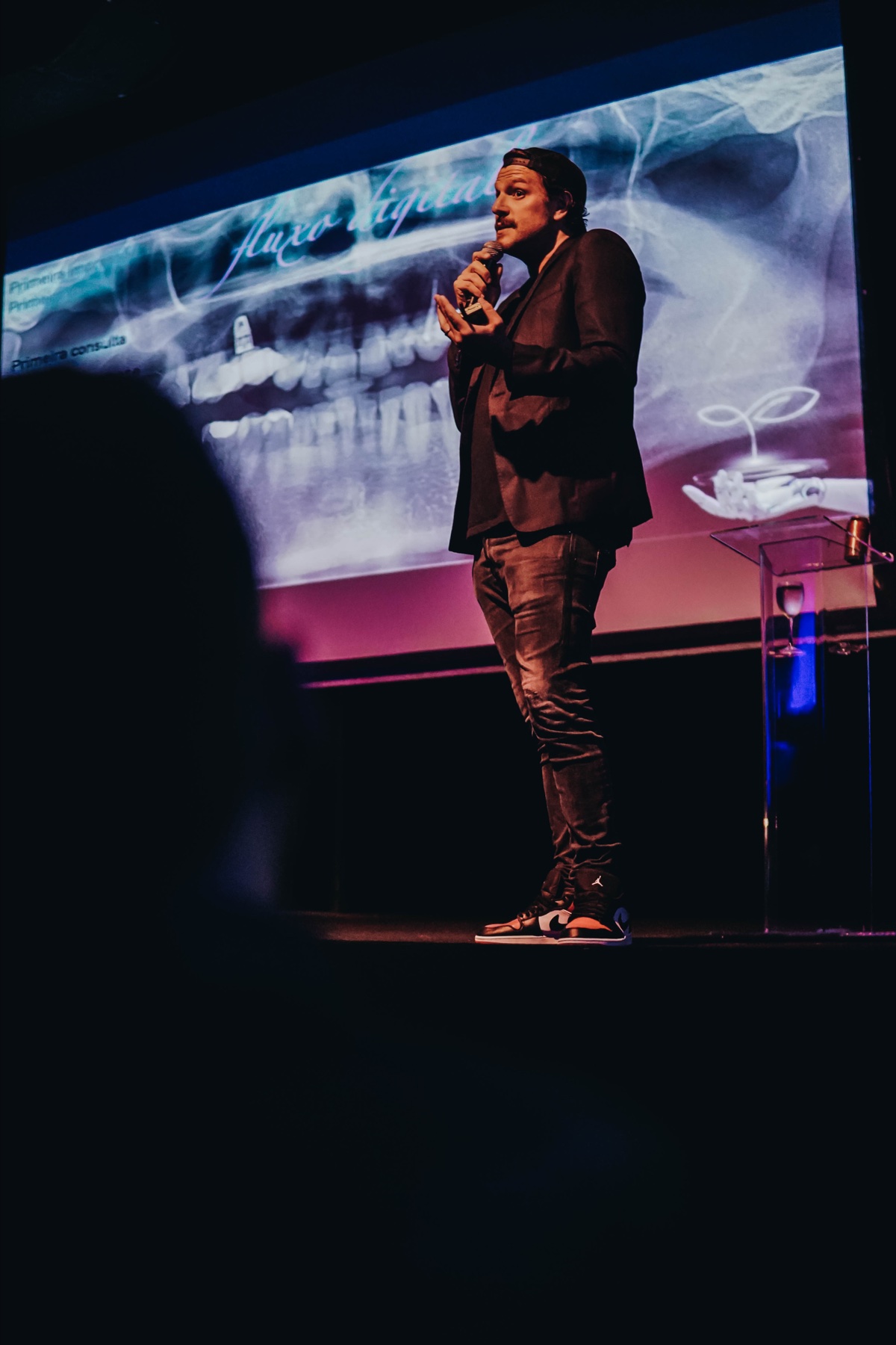 Rafa Puglisi no palco durante uma apresentação sobre odontologia.